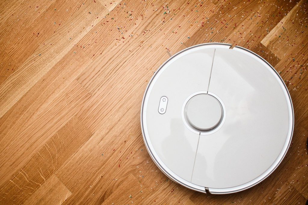 white robot vacuum on hard wood floor cleaning up sprinkles