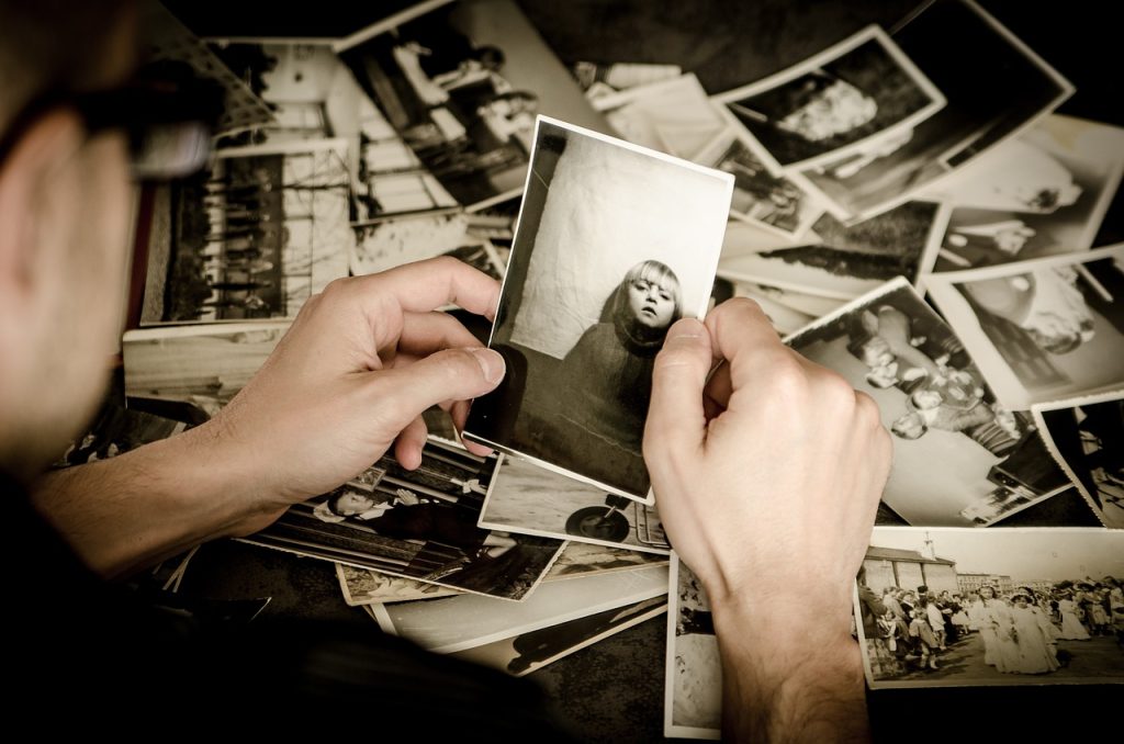 man holding black and white photos with more on the table behind him